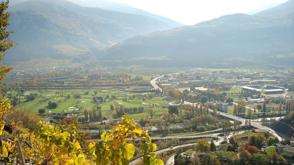 Vue aérienne d'une vallée avec une jonction autoroutière avec deux carrefours, des champs verts, des bâtiments et des montagnes en arrière-plan