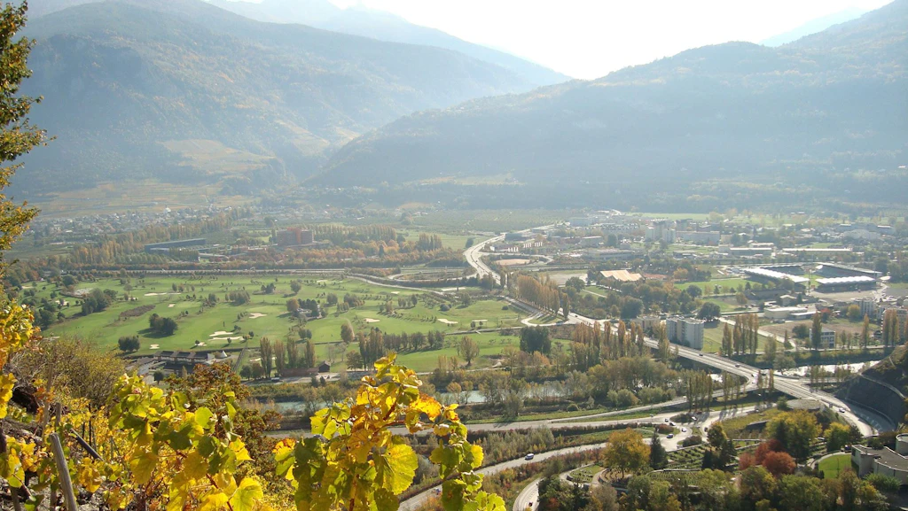 Vue aérienne d'une vallée avec une jonction autoroutière avec deux carrefours, des champs verts, des bâtiments et des montagnes en arrière-plan