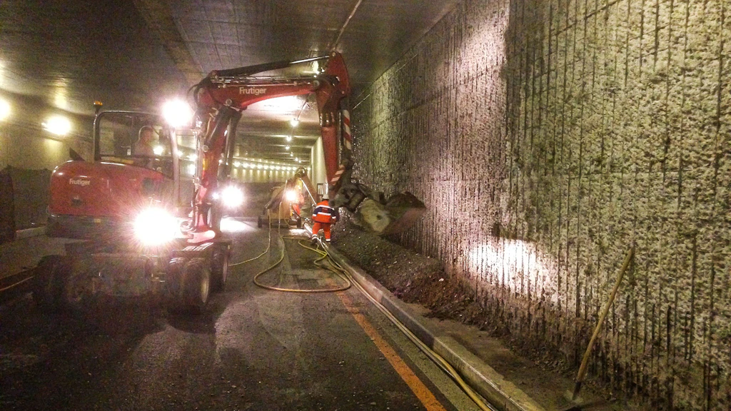 Baustelle in einem Tunnel mit Bagger und Bauarbeitern bei Sanierungsarbeiten an der Tunnelwand
