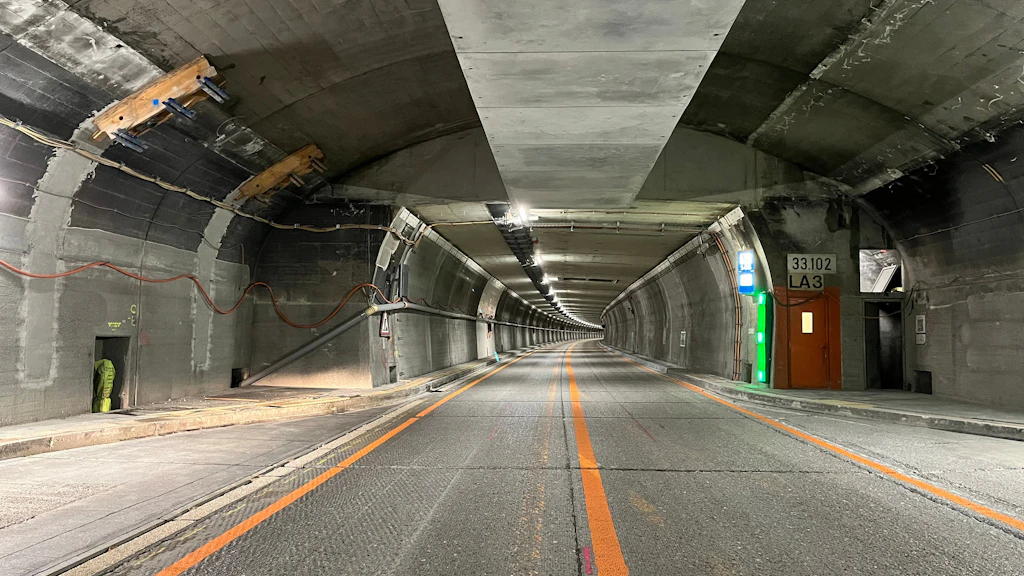Tunnelinnenraum mit Fahrbahn, orangefarbener Mittellinie und Notausgangstür an der rechten Wand
