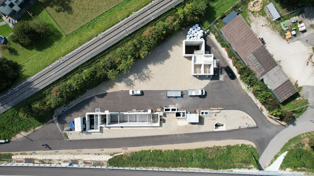 Luftaufnahme eines dreieckigen Platz zwischen Autobahn und Bahngleis mit mehreren Becken mit Betonmauern und Fahrzeugen