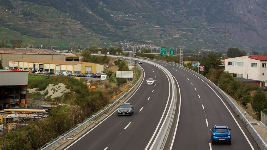 Vue aérienne d'une route à plusieurs voies avec quelques voitures et des bâtiments industriels en bordure. La chaussée est nouveau