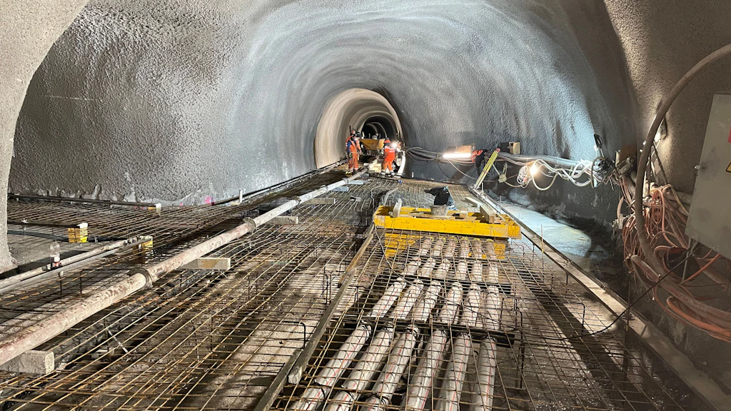 Ein Tunnel mit Stahlbewehrung und Baumaschinen auf dem Boden sowie Bauarbeiter im Hintergrund.