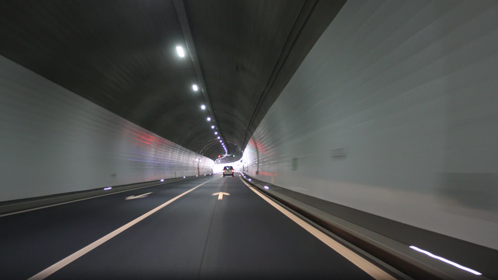Blick in den sanierten Rugentunnel mit glatten weissen Wänden, beleuchtet von einer Reihe Deckenlampen, und einem Auto auf der Fahrbahn