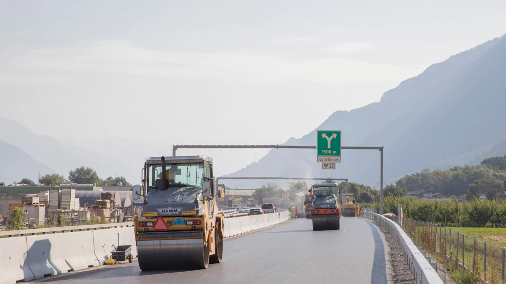 Deux rouleaux compresseurs sur une route en construction avec montagnes en arrière-plan