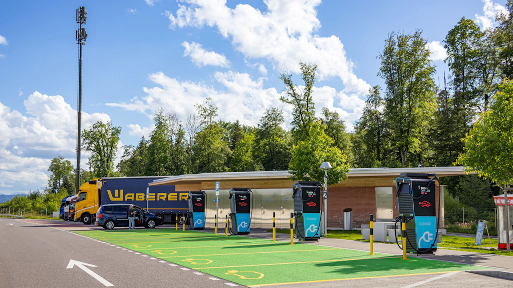 Schnellladestationen für Elektrofahrzeuge auf einem Rastplatz mit LKW und Wald im Hintergrund