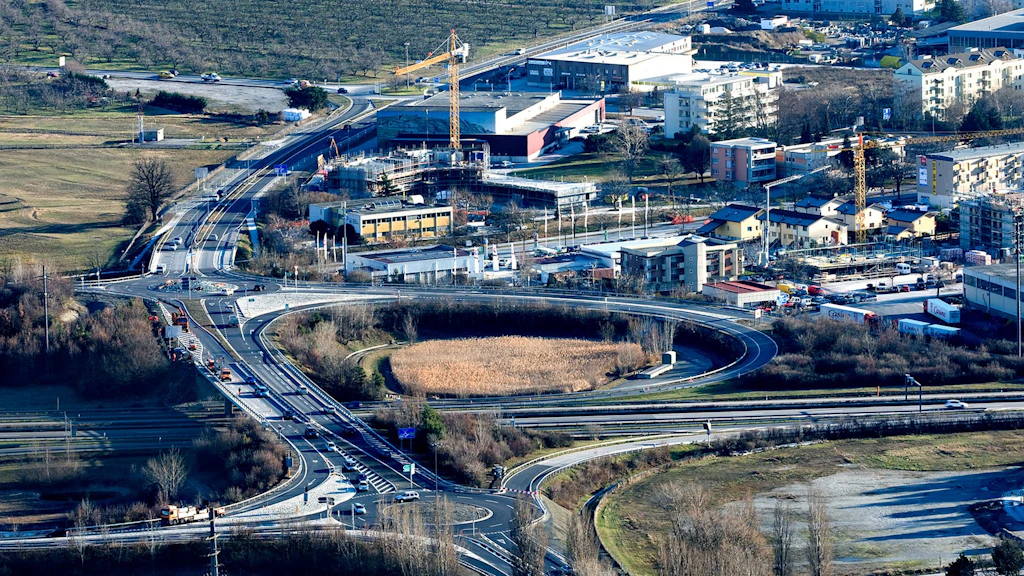 Vue aérienne d'une jonction autoroutière avec deux giratoires, entourée de bâtiments et de terrains dégagés