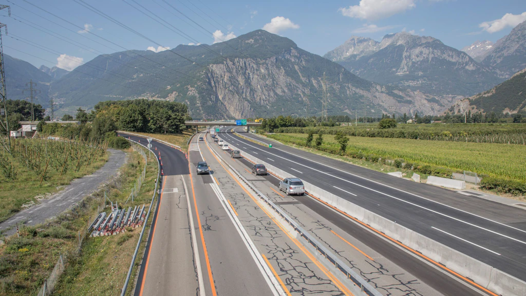 Autoroute à plusieurs voies avec voitures circulant en direction de montagnes en arrière-plan. À la gauche, la chaussée est vieille avec beaucoup de fissures est à la droite elle est assaini