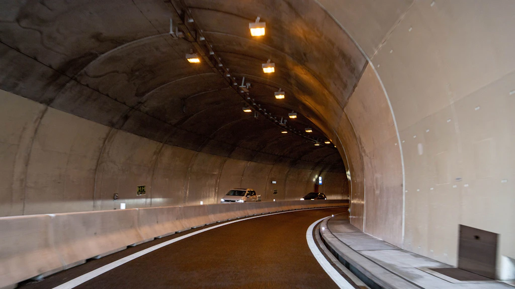 Tunnel avec un terre-plein central en béton et deux véhicules sur une chaussée sinueuse