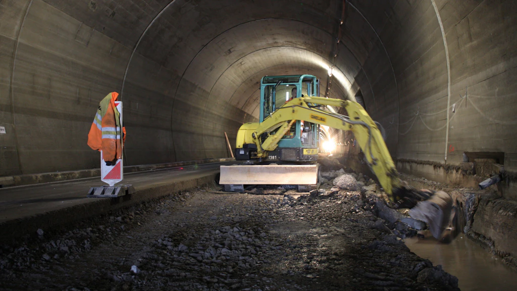 Une pelleteuse travaille à la surface du sol dans un tunnel aux parois et au plafond en béton