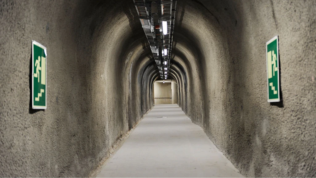 Petit tunnel voûté pour piétons, avec des parois rugueuses et deux panneaux verts indiquant les issues de secours sur les parois latérales.