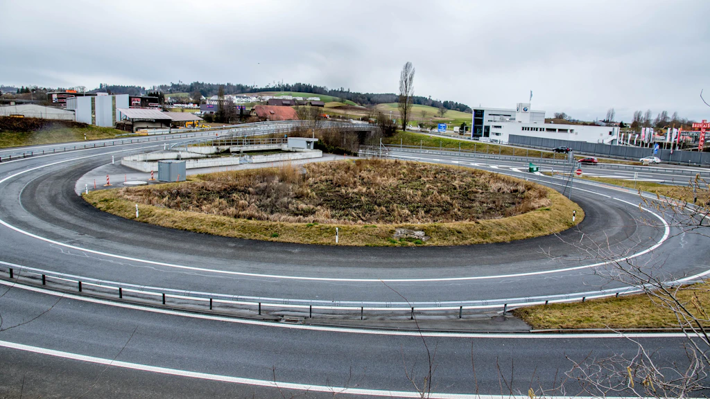 Kurve einer Autobahnausfahrt mit einem runden Wasserbecken in der Mitte. Das Becken ist mit Schilf bewachsen.