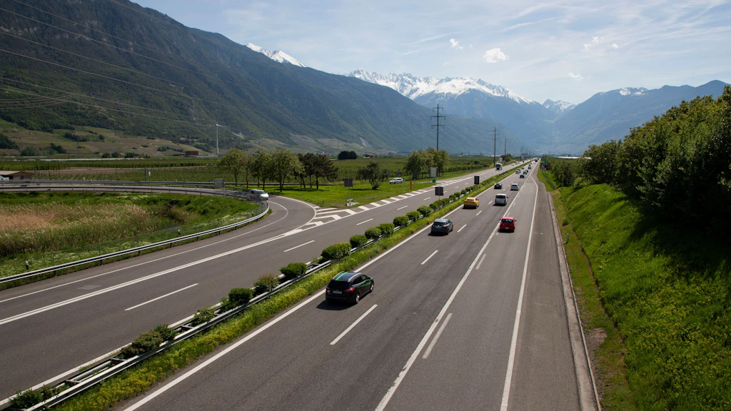 Autoroute à plusieurs voies traversant une vallée entourée de montagnes enneigées avec des voitures circulant dans les deux sens