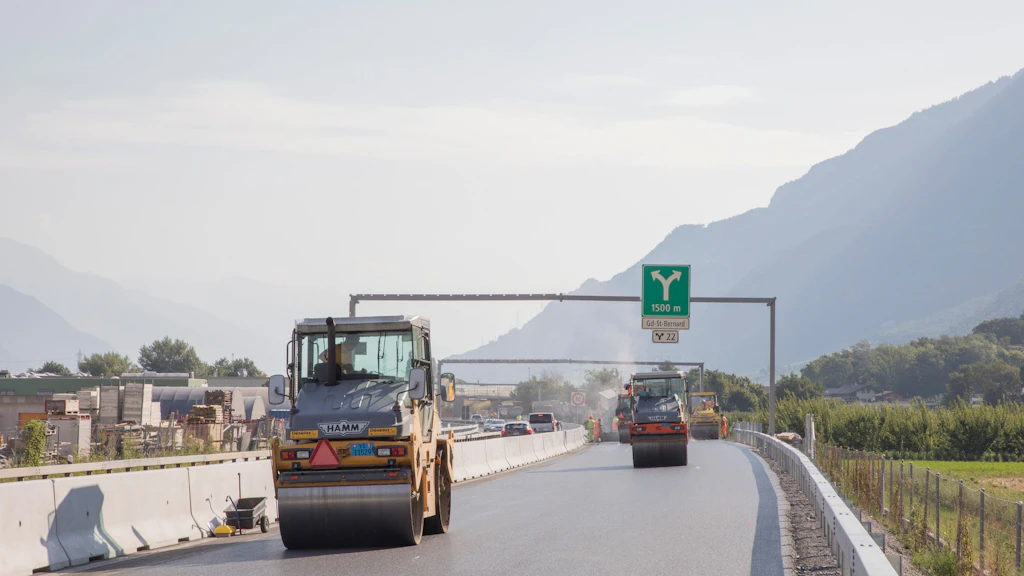 Deux rouleaux compresseurs sur une route en construction avec montagnes en arrière-plan
