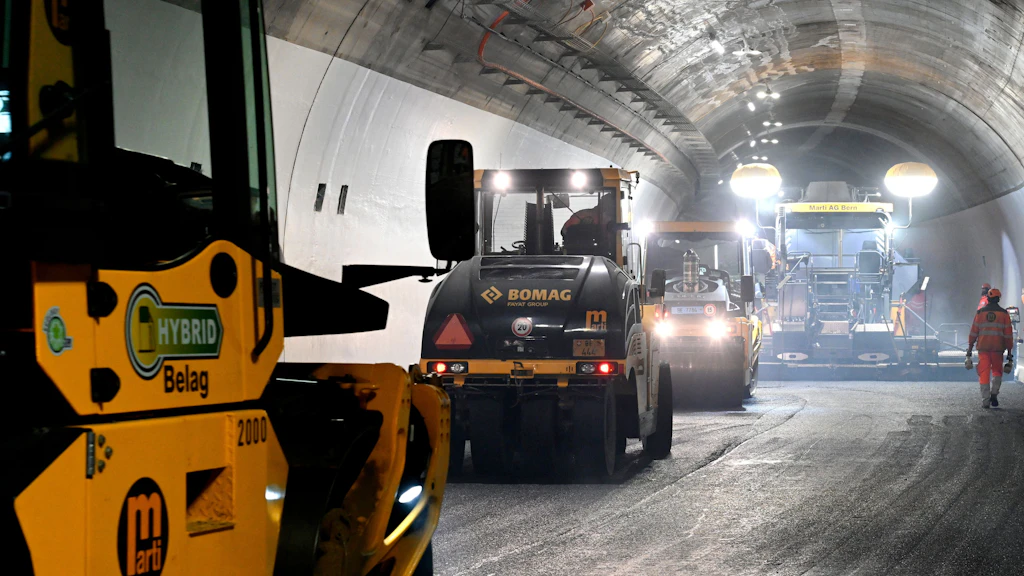 Strassensanierungsarbeiten in einem Tunnel mit mehreren Baumaschinen und einem Arbeiter in Warnkleidung